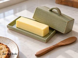 A sage green stoneware butter dish with the lid lifted to show the butter, made from The Clay Hole butter dish paper template