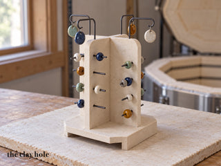 A handmade stoneware kiln bead tree with four fins on a hollow base, wire pins and hooks holding glazed beads and pendants, made from a Clay Hole paper template