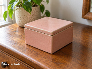 A small square pink stoneware keepsake box with a flat lid, made from The Clay Hole lidded box paper template