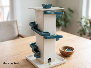 A white stoneware marble run tower with teal channels spiraling down it, made from The Clay Hole paper template