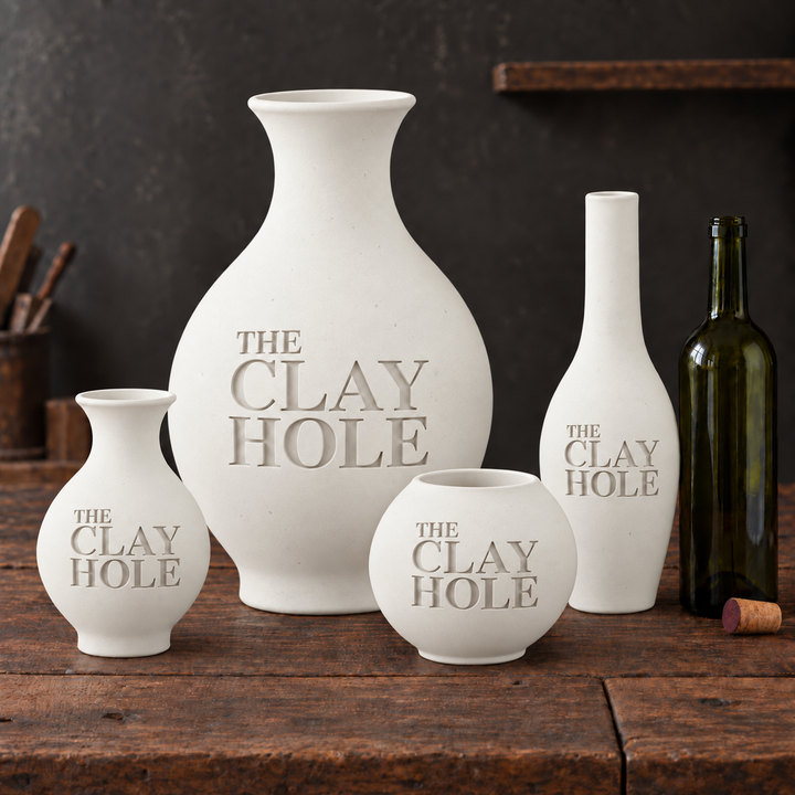 Four unglazed Laguna #16 Porcelain cone 6 clay vases stamped The Clay Hole, grouped with a wine bottle on a rustic table