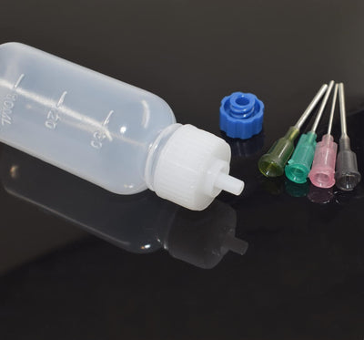 An applicator bottle lying on its side with a blue sealing cap and four needle tips