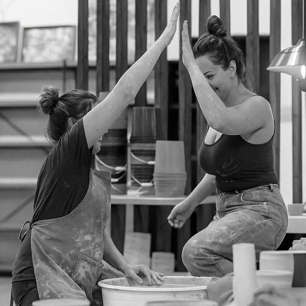 Two members high-fiving over their pottery wheels