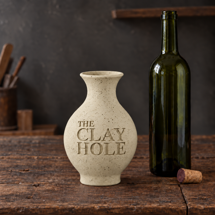 Unglazed cream Laguna B-Mix with Specks clay vase stamped The Clay Hole, beside a wine bottle on a wood table