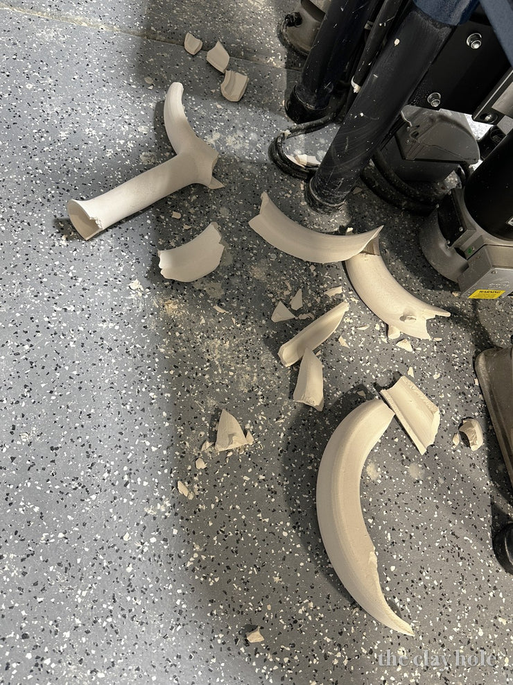 Broken unfired pottery shards scattered across a speckled studio floor