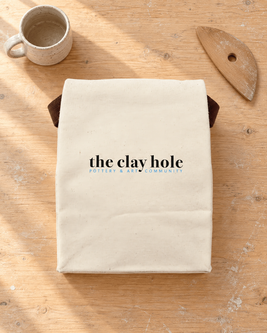 Natural canvas The Clay Hole tool bag with a brown strap, laid flat on a wooden studio table