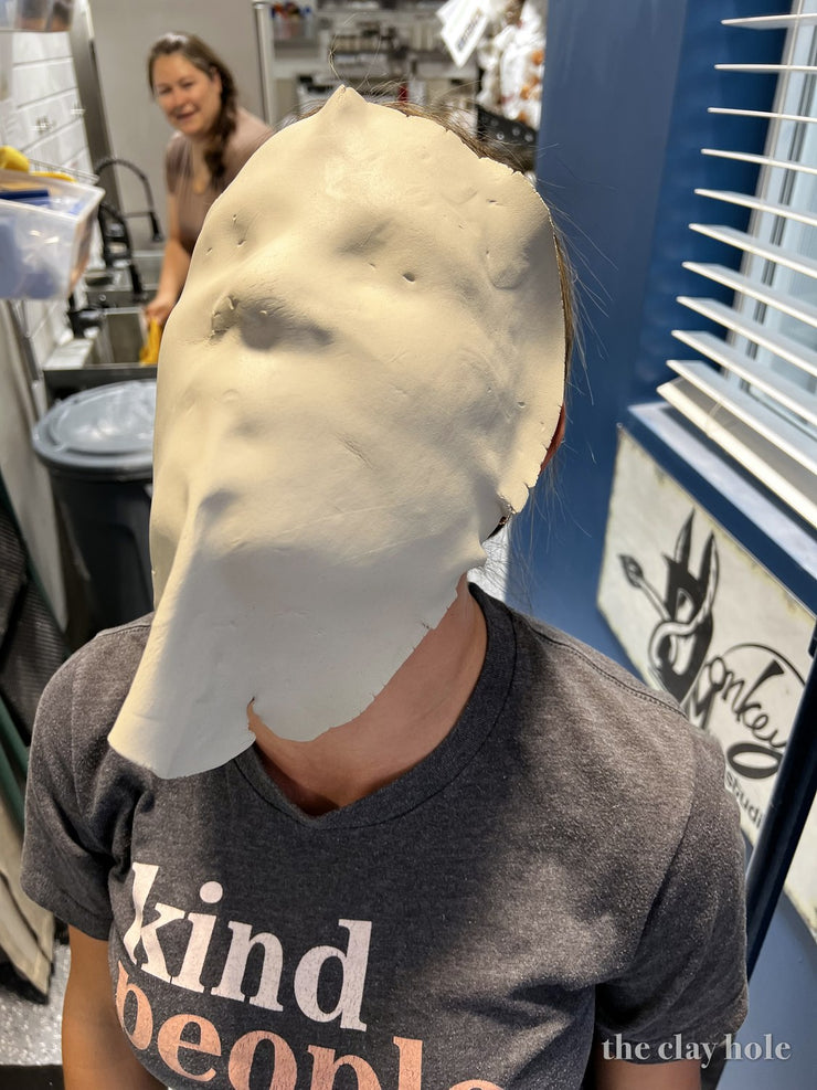 A slab of soft clay draped over a person's face like a mask in a pottery studio