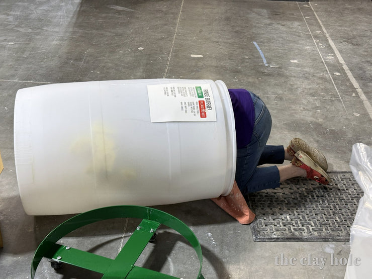 A person head first inside a large plastic rinse barrel, cleaning it out