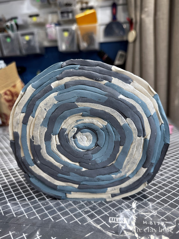 Spiral platter coil built from blue, gray and cream colored clay coils
