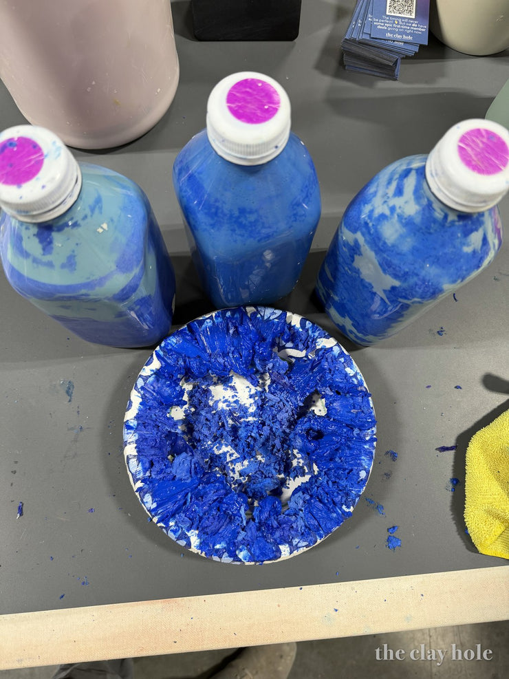 Plate of dried cobalt blue glaze flakes with bottles of blue glaze behind it