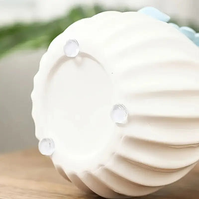 Four clear silicone bumper pads stuck to the foot ring on the bottom of a white fluted ceramic vase