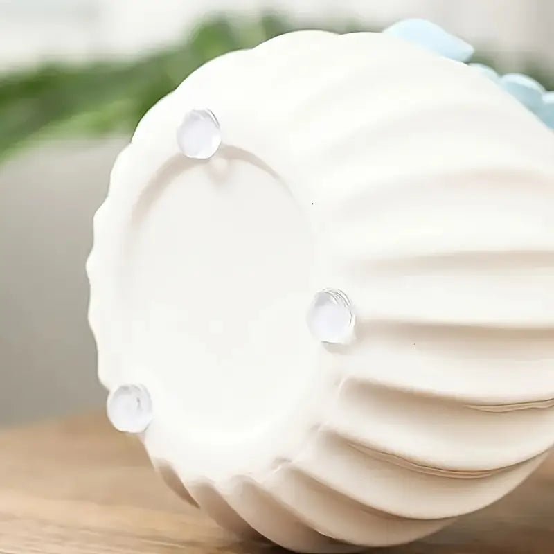 Four clear silicone bumper pads stuck to the foot ring on the bottom of a white fluted ceramic vase