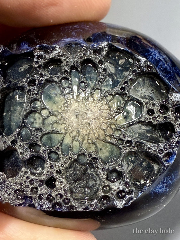 Macro photo of a fired glaze drop full of trapped bubbles, held between two fingers