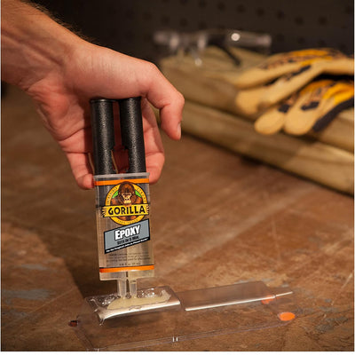 A hand pressing the plunger on a Gorilla epoxy syringe onto a mixing surface at a workbench