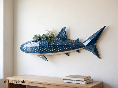 A faceted deep blue whale shark wall planter with white spots, made from The Clay Hole paper template, planted along its back