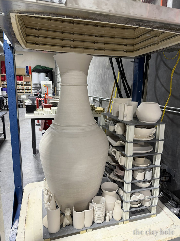 Giant floor vase and stacked shelves of pottery loaded into a large kiln with the lid raised