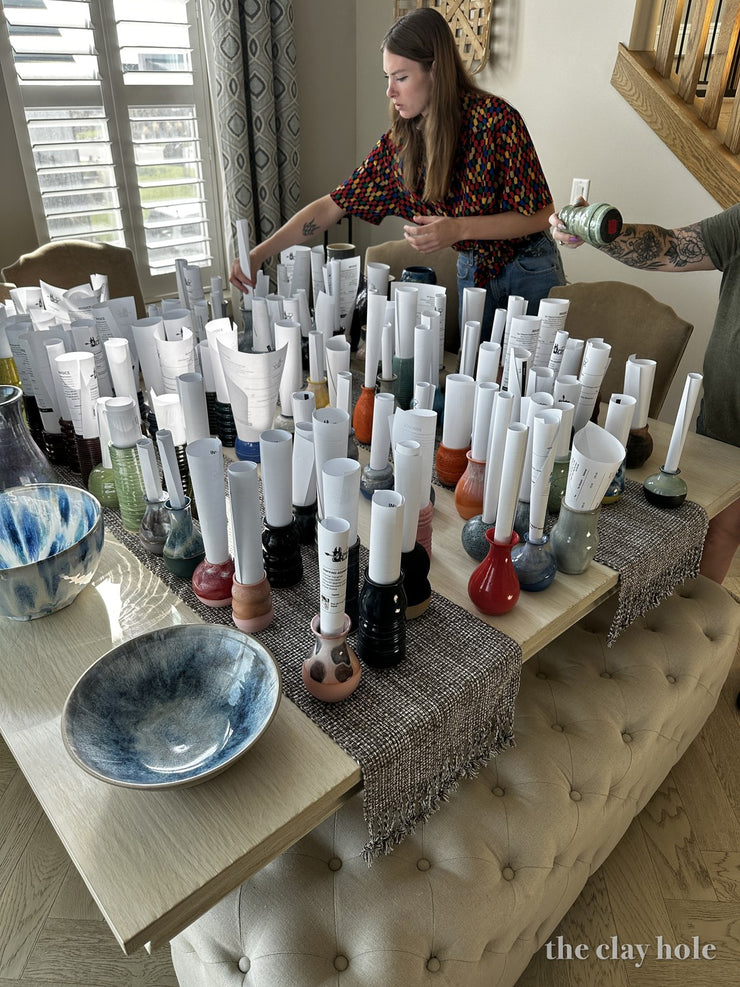 Table of small glazed bud vases, each one holding a rolled paper note