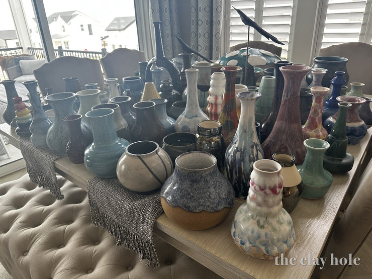 Table covered with dozens of finished glazed ceramic vases in many colors and shapes