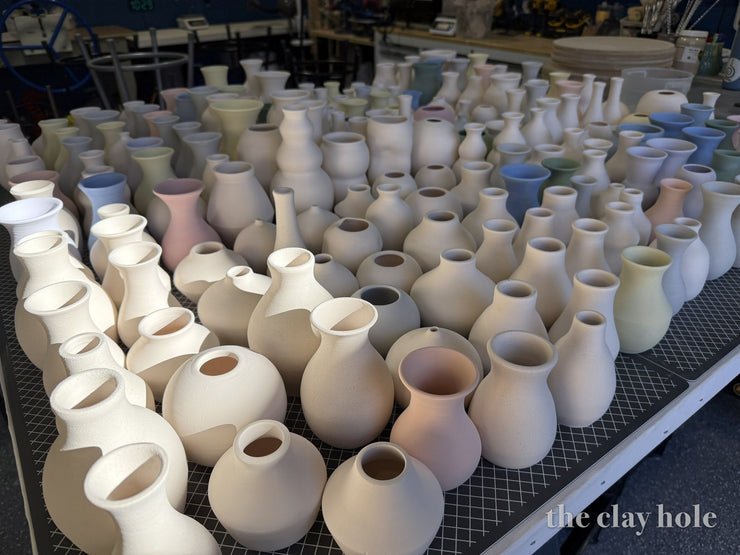 Studio table crowded with handmade bud vases in soft colored clays before glazing