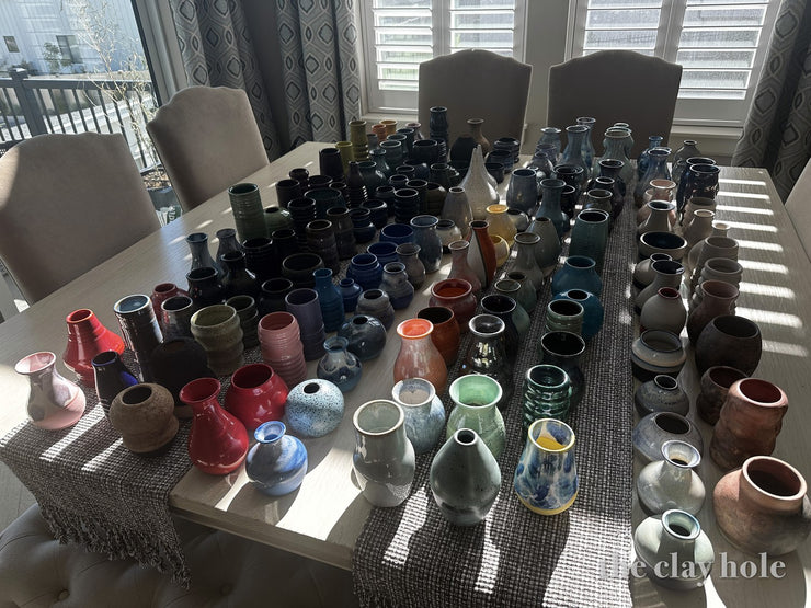 Dining table covered edge to edge with handmade pottery vases in low sunlight