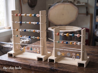 Two handmade stoneware kiln bead racks, a tall one and a small one, with glazed beads on white alumina rods, made from a Clay Hole paper template