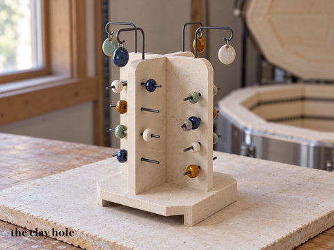 A handmade stoneware kiln bead tree with four fins on a hollow base, wire pins and hooks holding glazed beads and pendants, made from a Clay Hole paper template