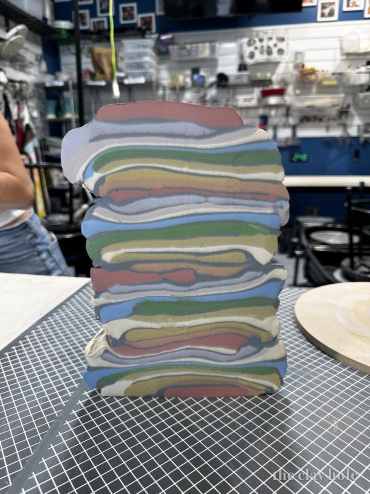 Tall block of layered colored pottery clay stacked up like striped sediment