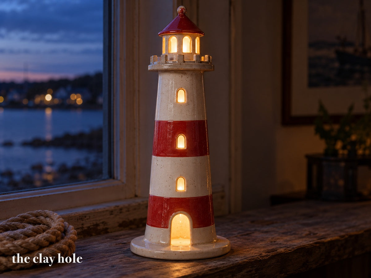 A tapered stoneware lighthouse lantern made from The Clay Hole paper template, its lantern room glowing