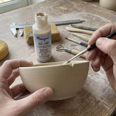 A potter brushing Mayco AC-306 Clay Mender into a crack on the side of a leather-hard stoneware bowl