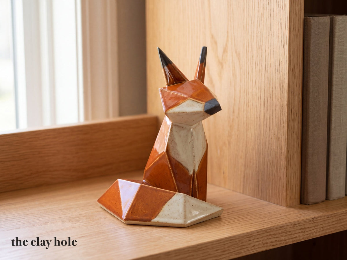 A handmade stoneware origami fox in burnt orange and cream, built from flat faceted slab pieces with a Clay Hole paper template