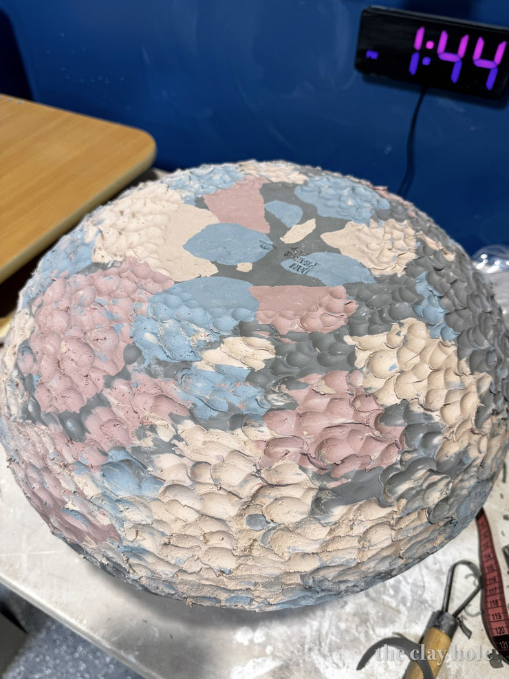 Dome of clay pinched into overlapping scales in pink, blue, gray and cream