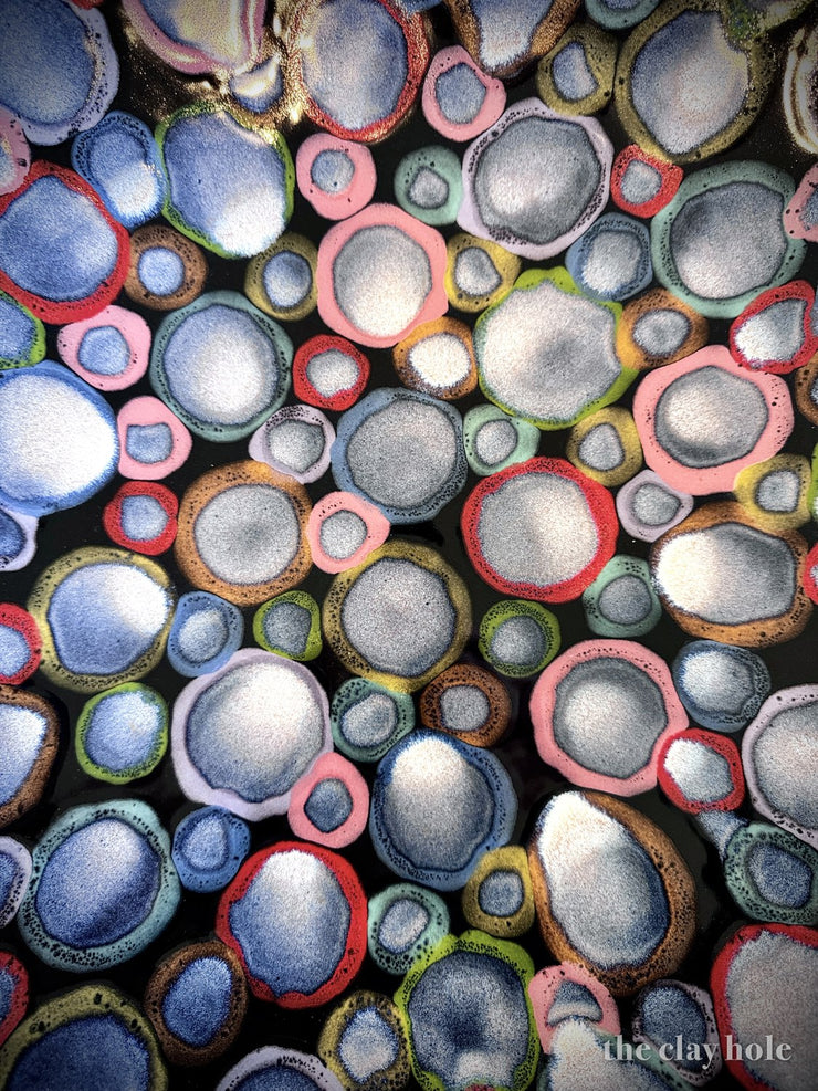 Fired pottery glaze pooled into colorful rings and circles on a dark surface, macro view