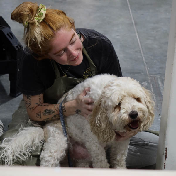 A Clay Hole member kneeling on the studio floor with both arms wrapped around Mud the studio dog while he leans into her