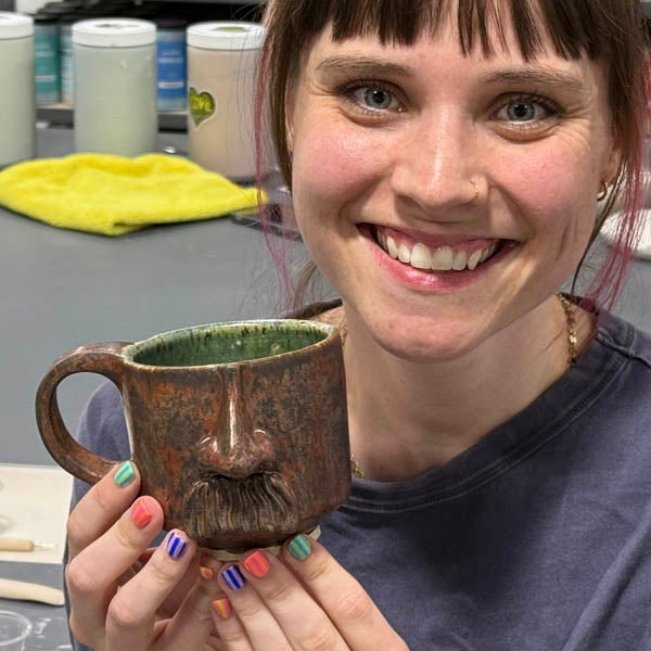 A Clay Hole member holding a finished glazed mug she made and fired at the studio