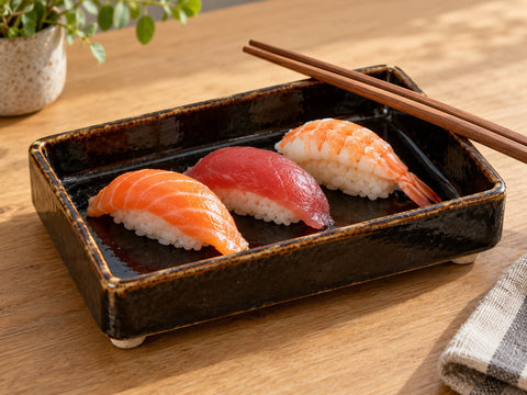 A folded black stoneware serving tray holding nigiri sushi, made from The Clay Hole folded tray paper template
