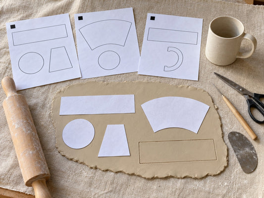 Printed paper pottery templates and paper cutouts on a rolled clay slab with tools and a finished mug, the all-fifteen bundle from The Clay Hole in Draper, Utah