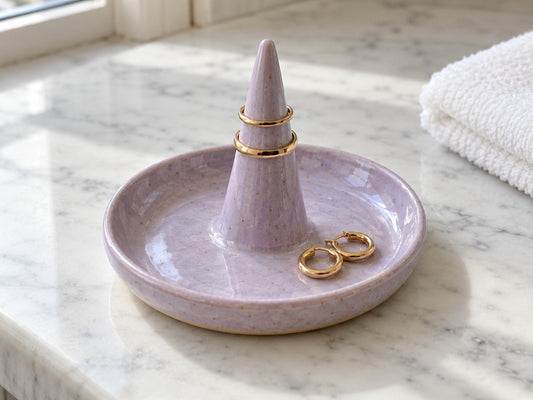 A lavender stoneware ring dish with a cone holding two gold rings, made from The Clay Hole ring dish paper template