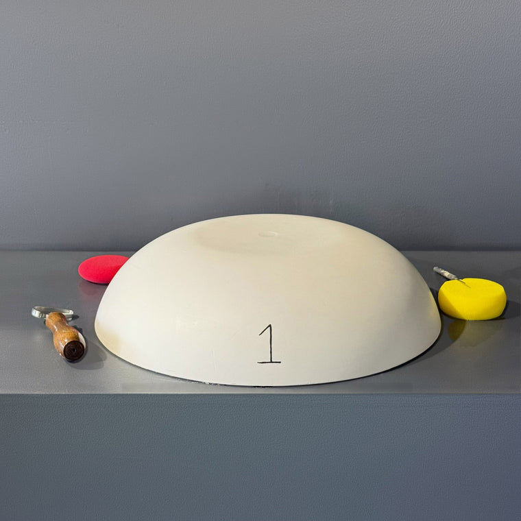 White pottery plaster hump mold number 1: a broad, shallow round dome, sitting rim-down on the gray studio shelf with a hand-written 1 on the front.