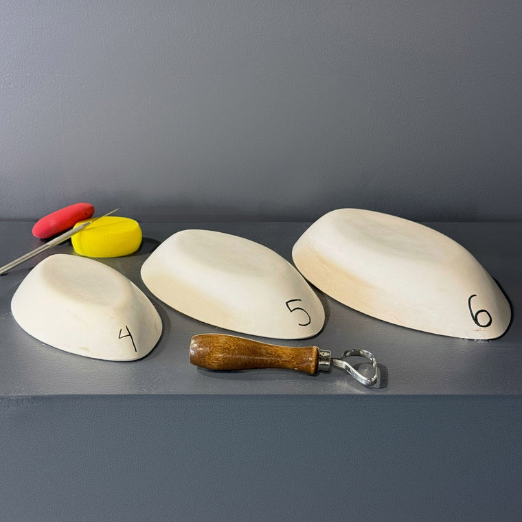 White pottery plaster hump mold number 4: a small rounded-triangular dome, the smallest of a trio shown together on the gray shelf.
