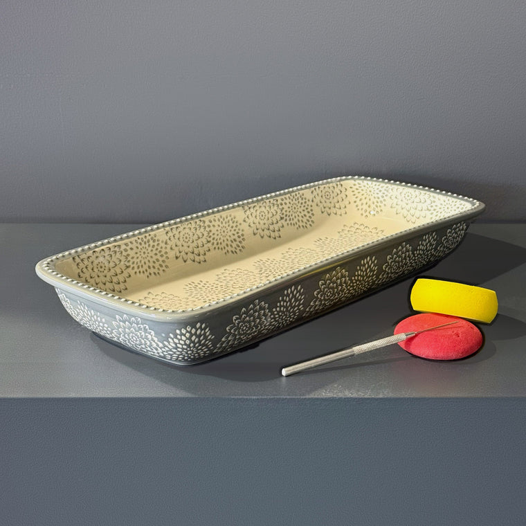 Glazed ceramic baking dish used as mold number 20: a long rectangular dish, glazed gray-blue with a band of white chrysanthemum relief around the outside walls, sitting right side up and open on the gray shelf.