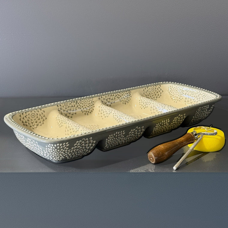 Glazed ceramic four-well mini loaf pan used as mold number 21: a rectangular pan, glazed gray-blue with white chrysanthemum relief around the outside, sitting right side up on the gray shelf with four loaf-shaped wells in a row.