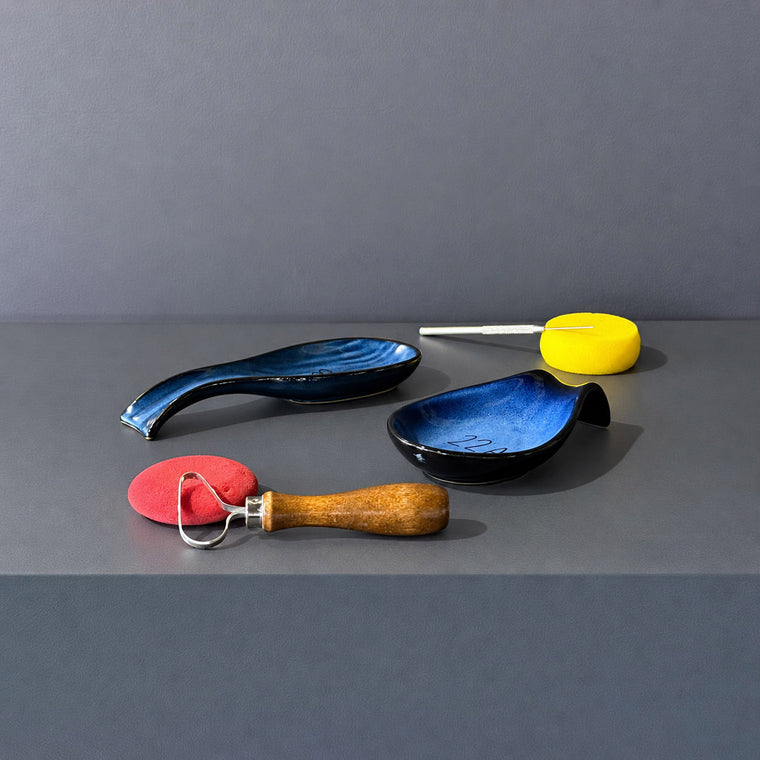 Blue glazed ceramic dish used as mold 22A: a small teardrop-shaped dish, turned upside down on the gray shelf beside a matching small bottle.