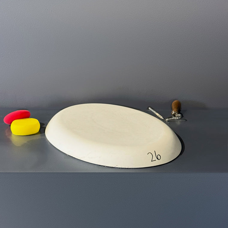 Large flat white plaster oval slab mold number 26: a nearly flat oval, lying on the gray shelf.