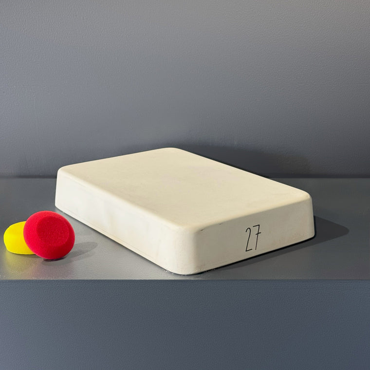 White pottery plaster mold number 27: a rounded rectangular block, set at an angle on the gray shelf.