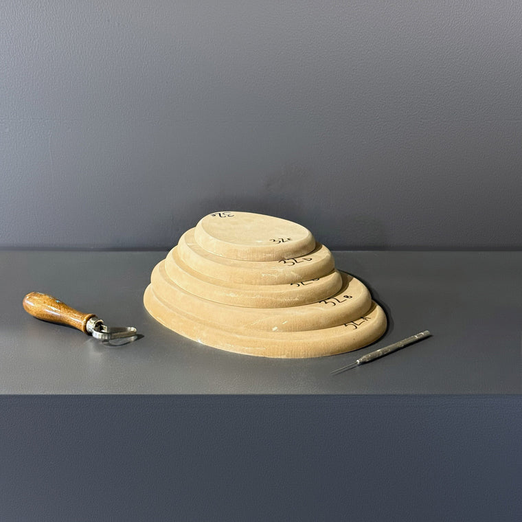 High-density fiberboard mold 32A: a flat oval disc, the largest of a 5-piece nesting set shown stacked largest to smallest on the gray shelf, hand-labeled 32A.