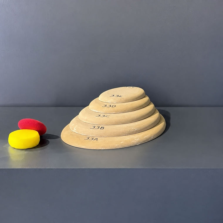 High-density fiberboard slab mold 33A: a flat oval disc, the largest of a five-piece nesting set shown stacked largest to smallest on the gray studio shelf, each piece hand-labeled 33A through 33E.