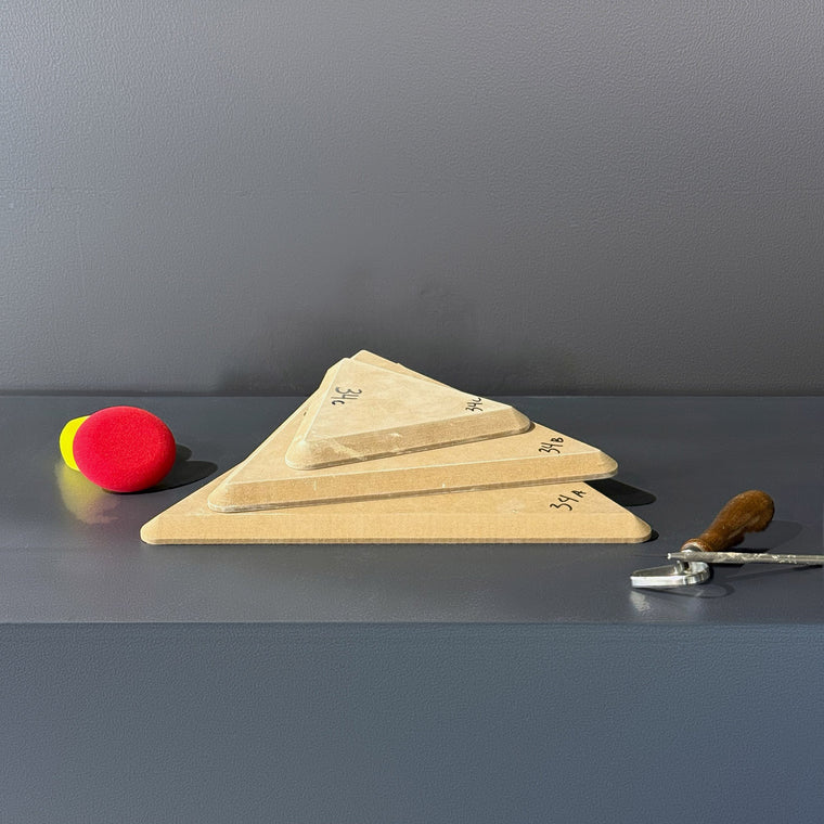 High-density fiberboard mold 34A: a rounded triangular board, the largest of a 3-piece nesting set shown stacked largest to smallest on the gray shelf, hand-labeled 34A.