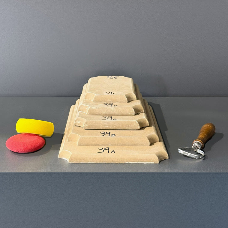 High-density fiberboard mold 39A: a square board with a softly waved edge, the largest of a 5-piece nesting set shown stacked largest to smallest on the gray shelf, hand-labeled 39A.
