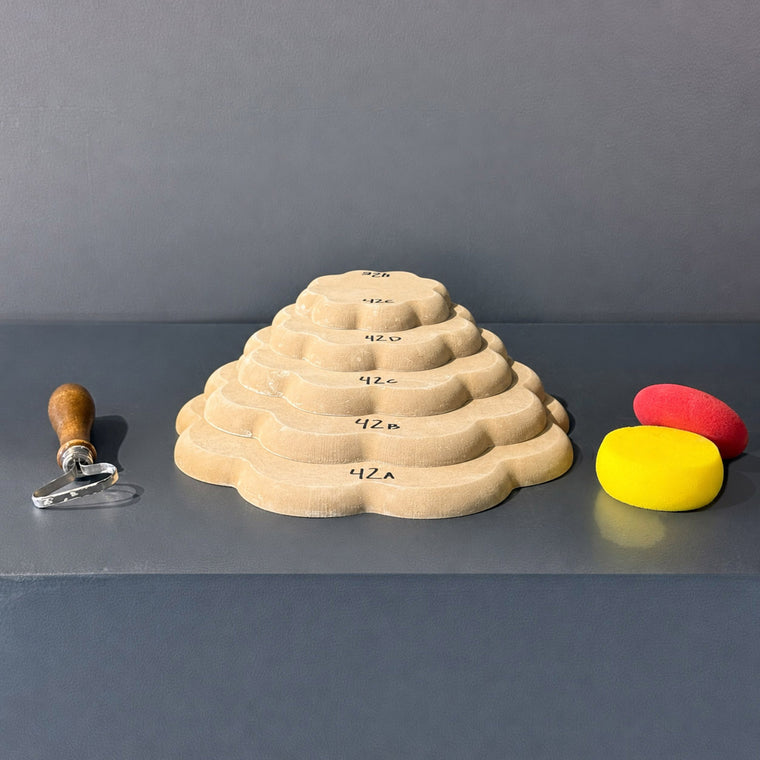 High-density fiberboard mold 42A: a scalloped flower-shaped board, the largest of a 5-piece nesting set shown stacked largest to smallest on the gray shelf, hand-labeled 42A.