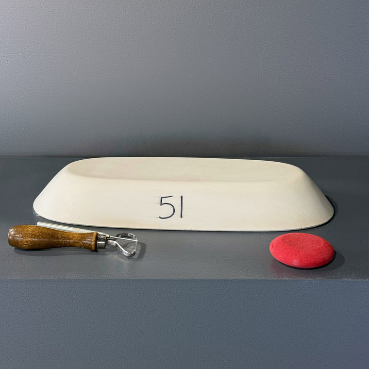 White pottery plaster hump mold number 51: a long stadium-shaped oval dome, set at a slight angle on the gray shelf.